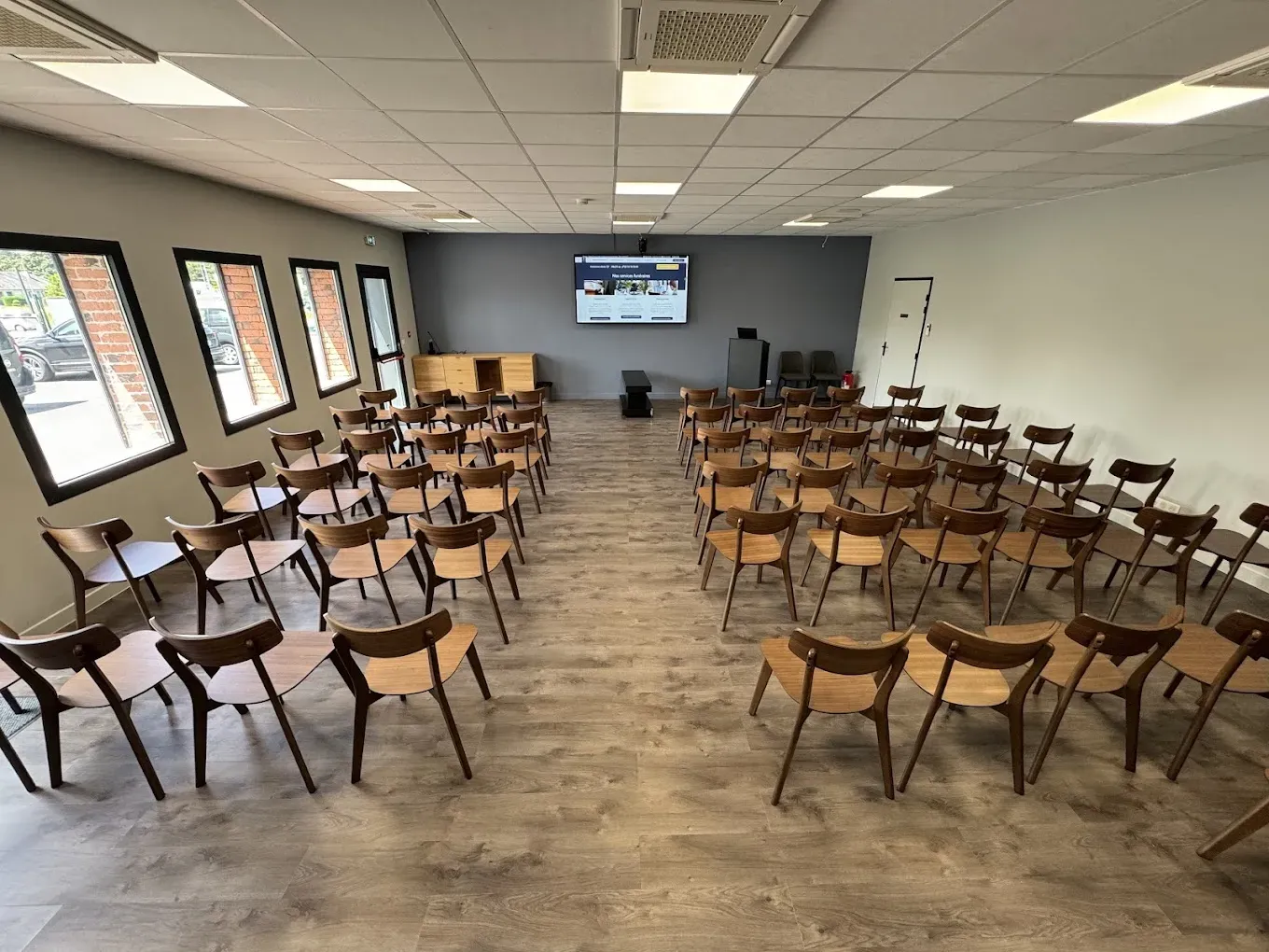 Salle d'hommage et d'assemblée équipée de rangées de chaises en bois et d'un écran mural.